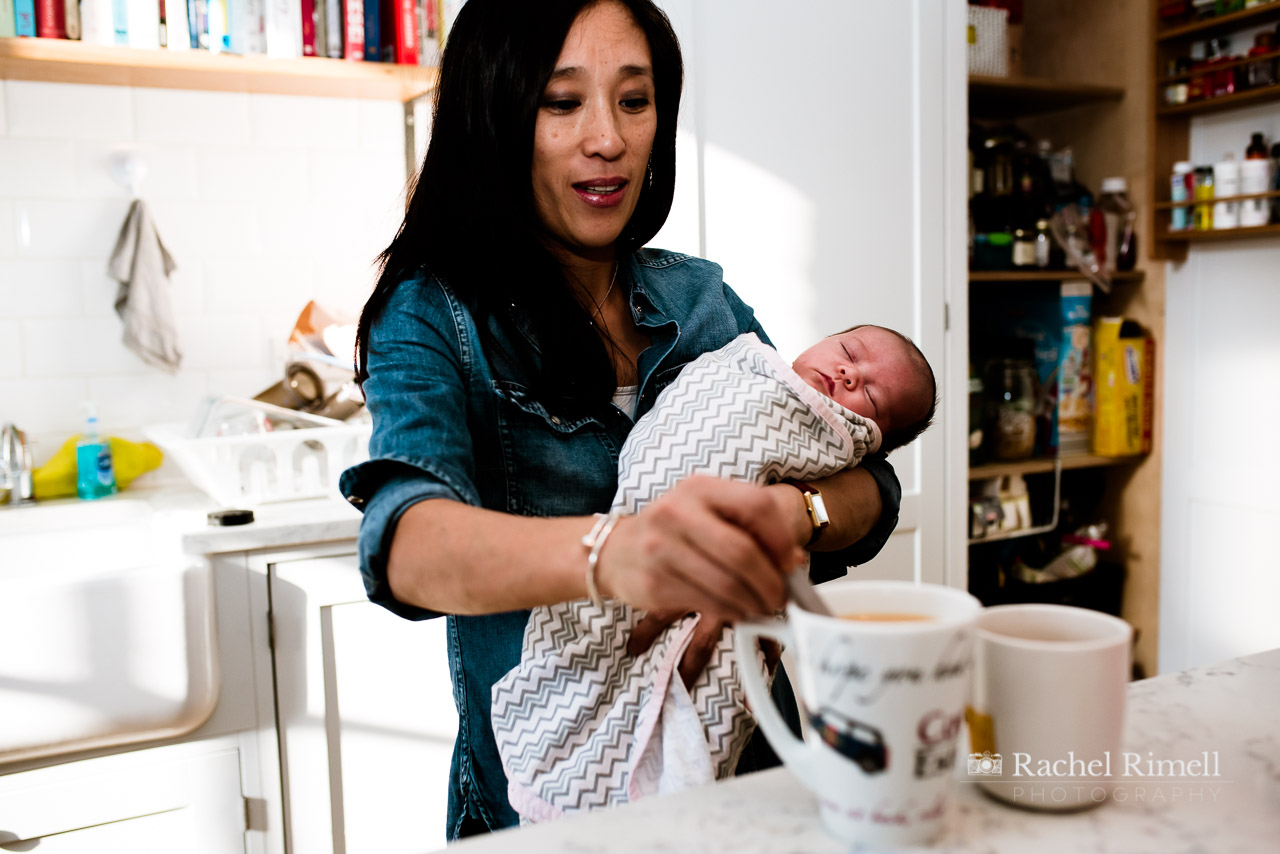 Mother makes a cup of tea while holding newborn baby natural portrait London