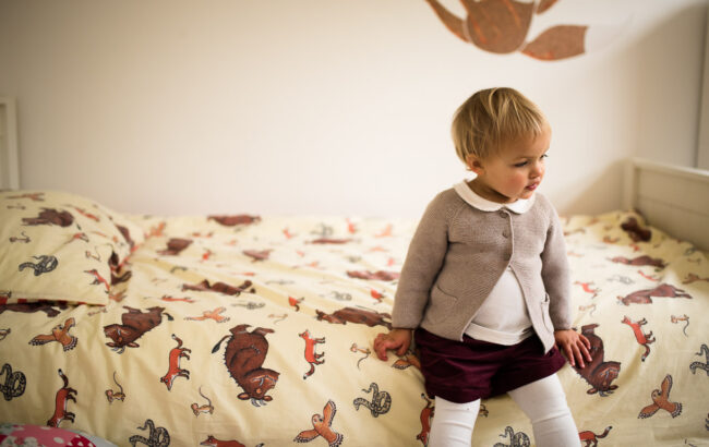 Unconventional child portrait of girl sitting on her bad with Gruffalo bedding on a day in the life fun unposed family photography day in Blackheath