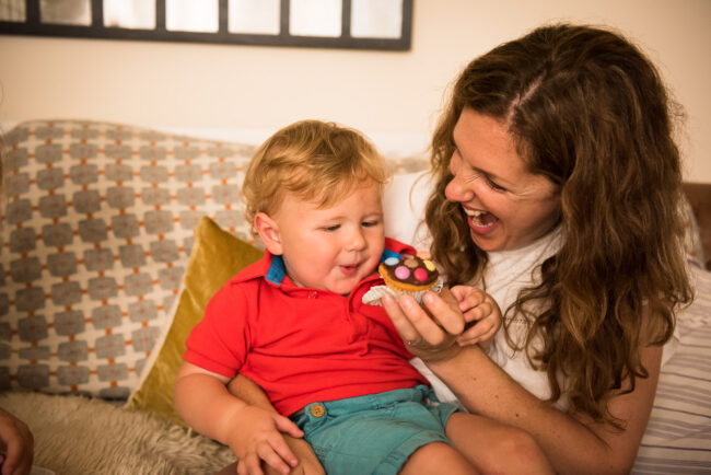 candid portrait of mother feeding her son a colourful cupcake on their sofa at an in home relaxed day in the life family photography session in London