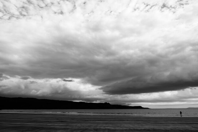 fine art landscape photography print - black and white image of solitary figure on the beach with dramatic cloudy sky