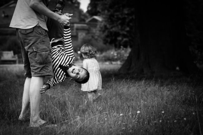 father dangling son upside down in candid family photo in Greenwich Park