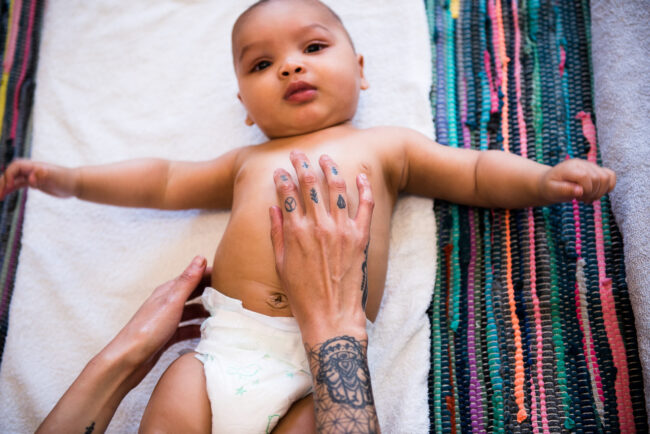 baby during a baby massage class with mums tattooed hands