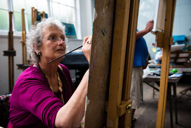 editorial photo of artist working in an art class at Blackheath Conservatoire painting at an easel wearing a cerise jumper