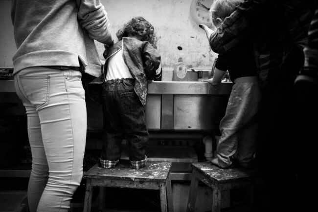 black and white photo of children washing up at an art class with parents legs in frame at Blackheath Conservatoire on a business photography session