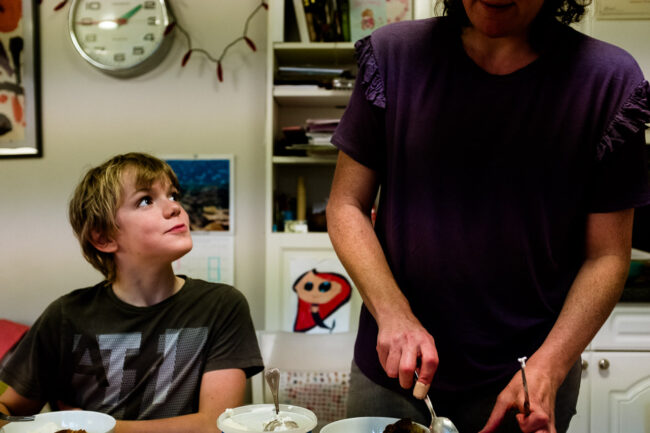 teenage boy looks up at his mum and she serves him ice cream in their kitchen in North London candid portrait