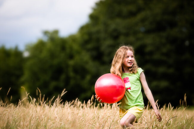 girl in a green t-shirt in long grass at Brockwell Park with a large red ball natural child portrait