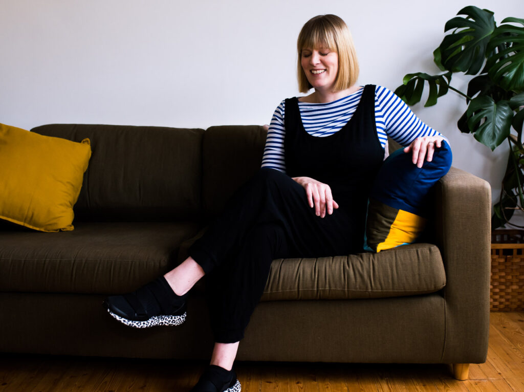 Fun relaxed professional branding portrait of life coach Janine Green laughing on her sofa with yellow cushions in Crystal Palace, London