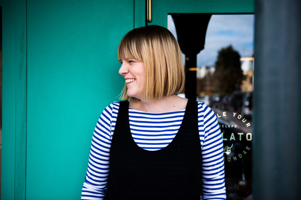 Fun and relaxed natural professional headshot of Janine Green in Crystal Palace with teal background, laughing