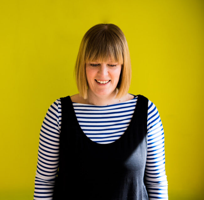 relaxed headshot of Janine Green Coach at her home in Londn against green background in stripy top for personal branding photography session