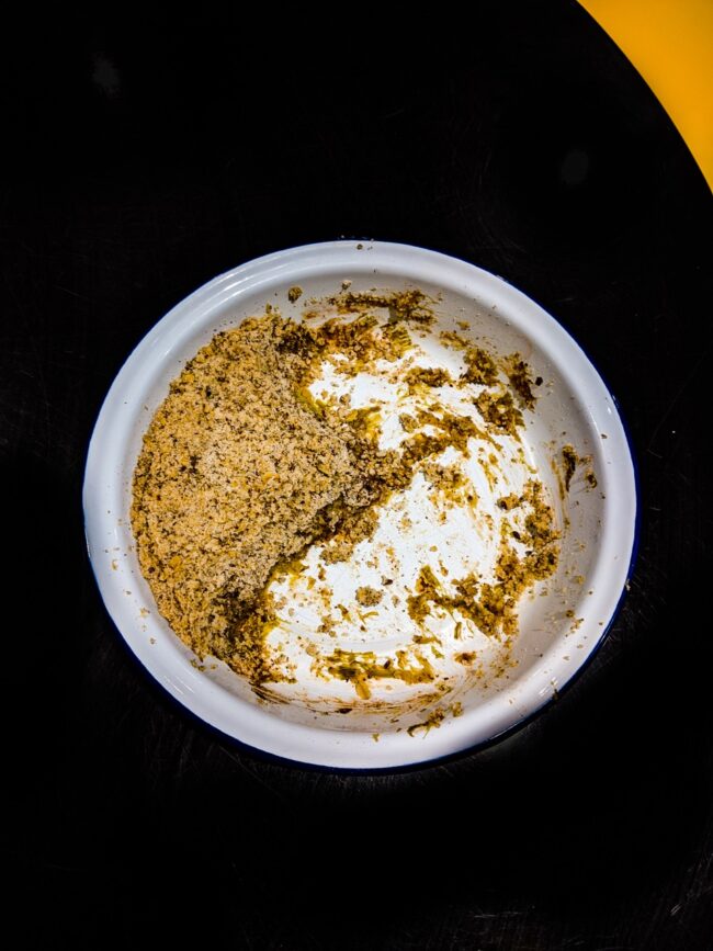 Stylistic food photo of half eaten crumble in an enamel dish on a black table background with a curve and small triangle of yellow, London