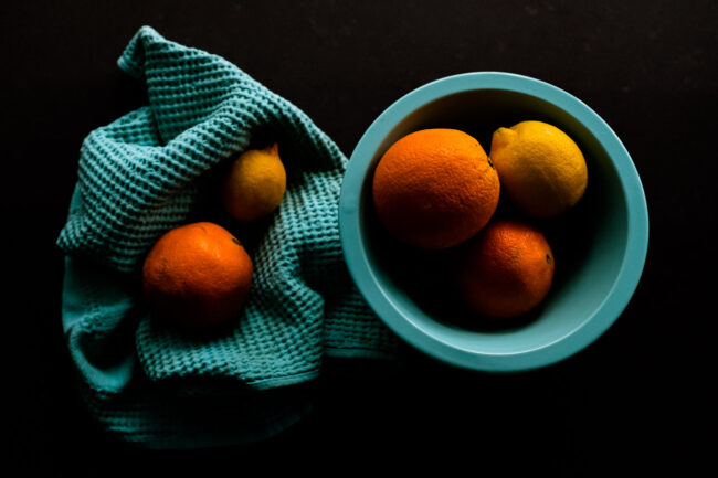 creative styled food photo of oranges and lemons in a turqoise bowl and tea towel on black background