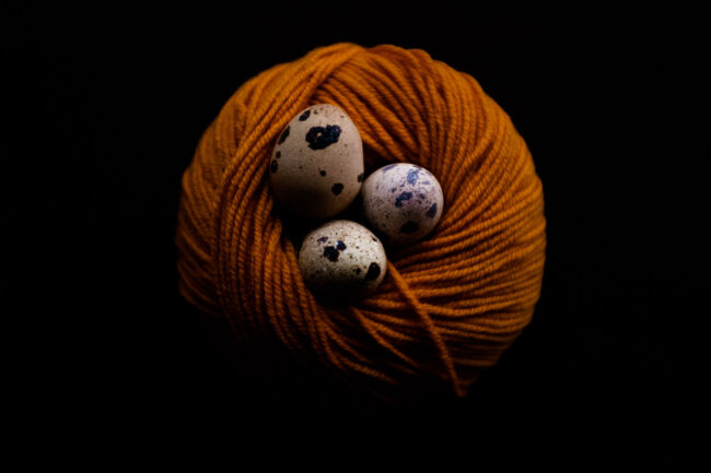 styled food shot of quails eggs in a nest made of a yellow ball of wool on black background, London