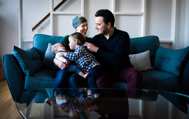 relaxed family portrait with mum in headscarf, dad, baby and big sister on a blue sofa in Forest Hill London