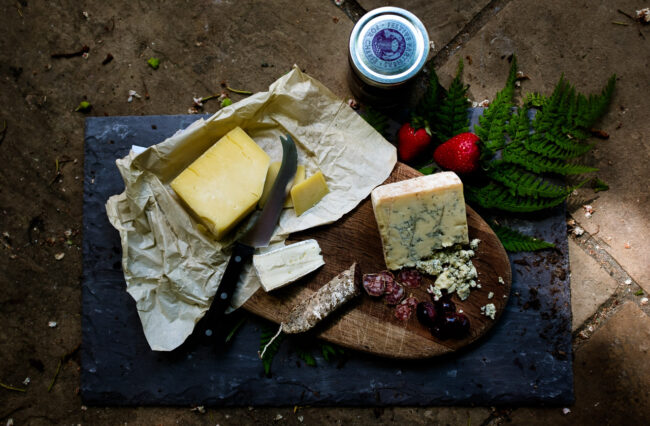 flat lay of cheese selection and salami with fern leaf and strawberries