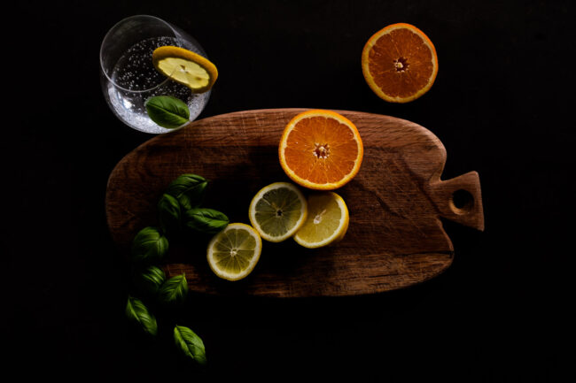 Stylised food photography image of oranges and lemons on a wooden choppung board with scattering of basil and a glass of gin with a slice of lemon, London