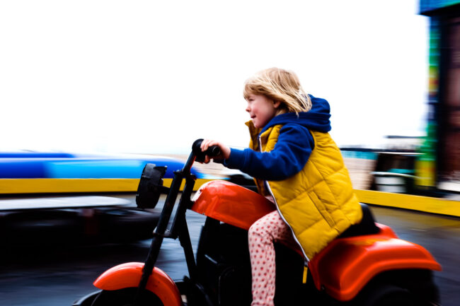 Girl in yellow jacket on a red bike at a fairground ride