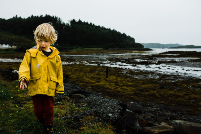 Boy walking across a seaweed beach in Mull