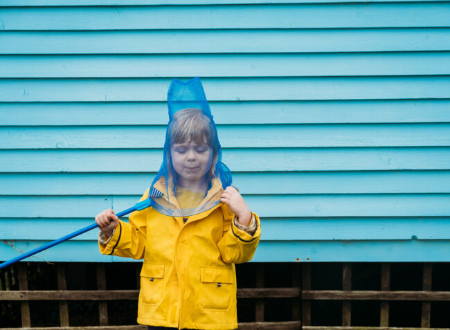 Girl in yellow raincoat with a blue fishing net on her head and blue background