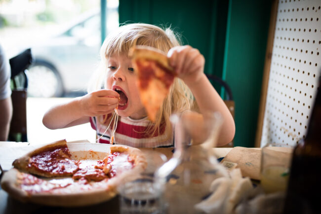 candid and alternative family photography image of girl eating pizza in Crystal Palace, London in a stripy dress