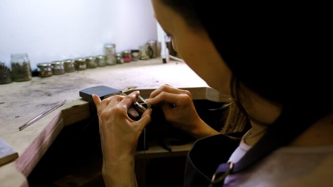 editorial portrait of jewellery maker working on a pendant fitting at her jewellers table in Crystal Palace studio
