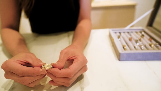 close up detail image of a gold and diamond ring with hands close up in the frame with box of rings in the background at studio of Untold Jewellery in Crystal palace London