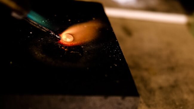 close up detail image of a piece of gold being melted with a blow torch on a jeweller's bench in Crystal Palace, London