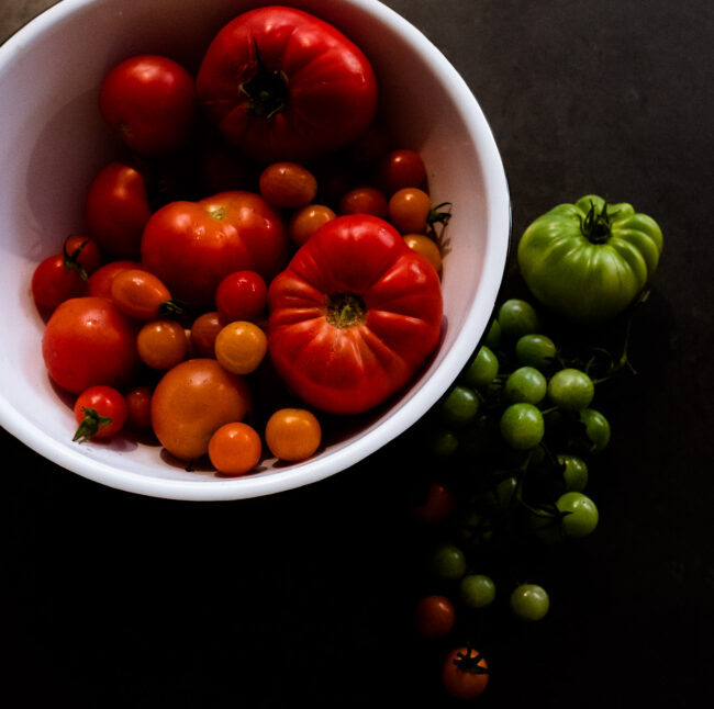red tomatoes in a white bowl with green tomatoes on a black background styled food photo