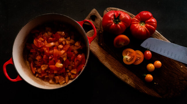 flat lay photo of tomato chutney in a red Le Creuset pot with tomatoes on a chopping board