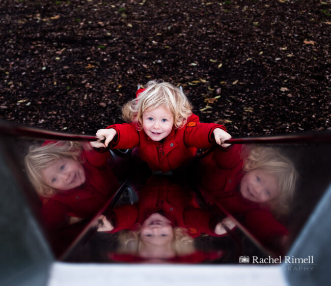 child portrait of a boy on a slide reflected in the sides of the metal slide