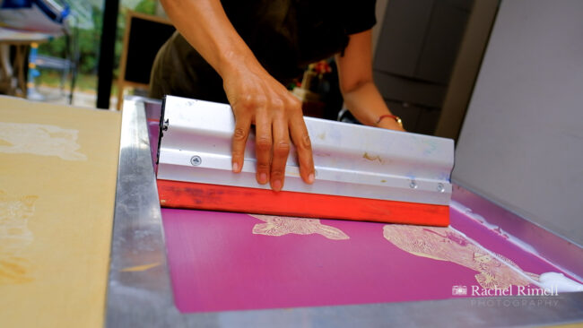 detail of textile artist screen printing a pig pattern onto fabric