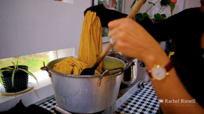 textile artist in her studio natural dying cloth with onion skin dye pulling up yellow liquid from hot pot