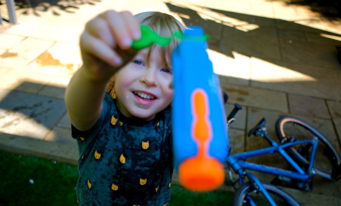 Boy holds a water pistol to the camera for a family photo