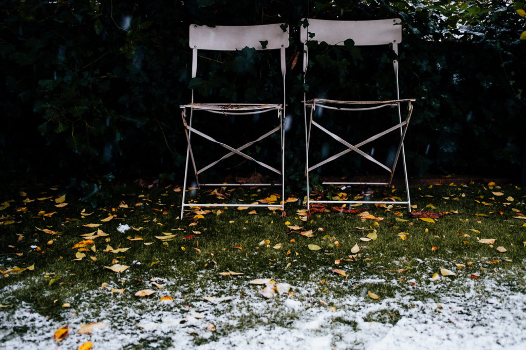 two white deck chairs in the snow with falling snow