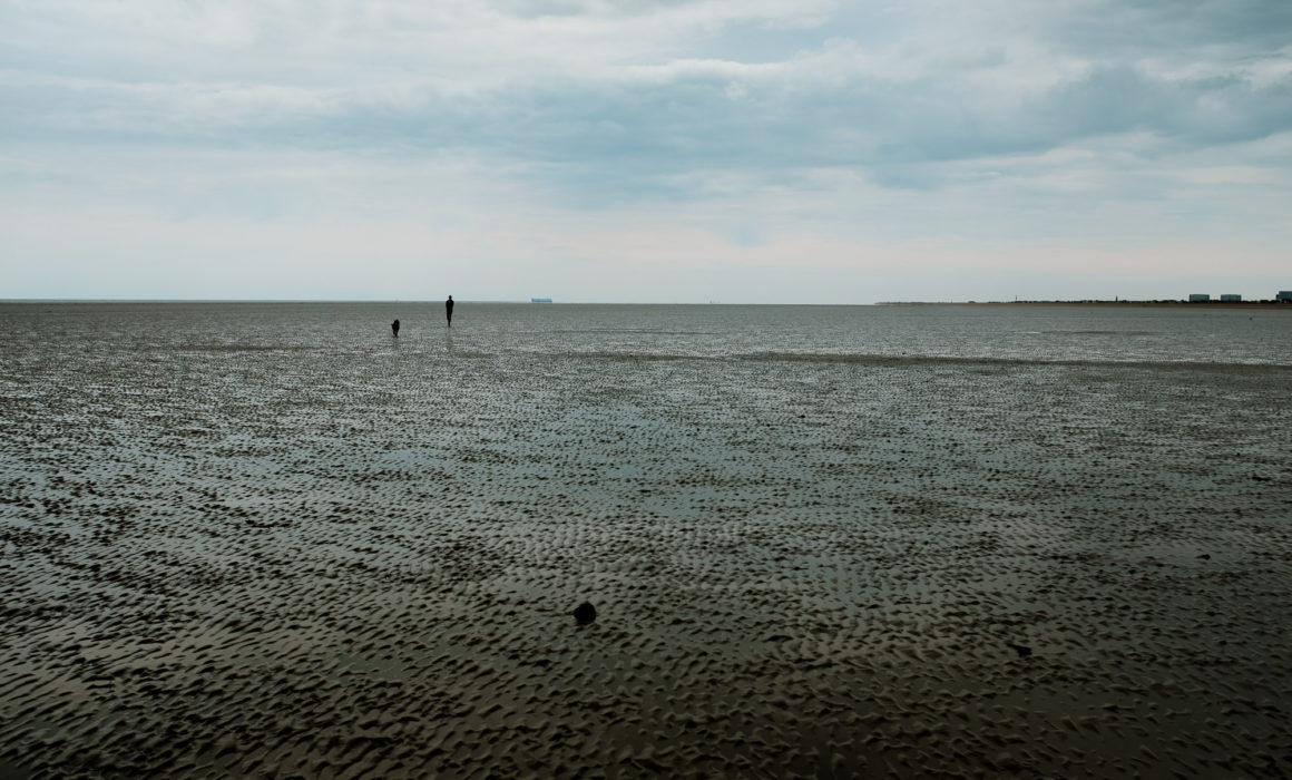 silhouette figures of man and dog on the beach at Greatstone with the tide out