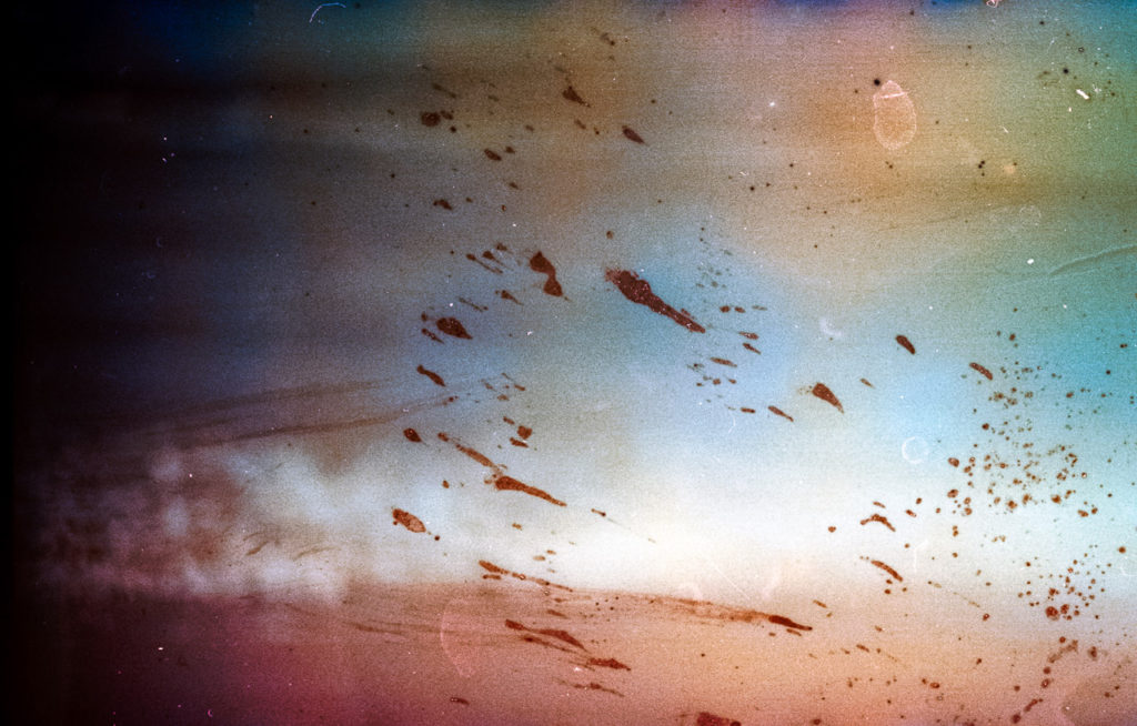 semi abstract image of waves in the background in pinks and pale blue hues with marks and scratches caused by immersing the 35mm film in seawater before developing so that salt crystallises on the final negative. Taken at Hunmanby Gap, North Yorkshire.