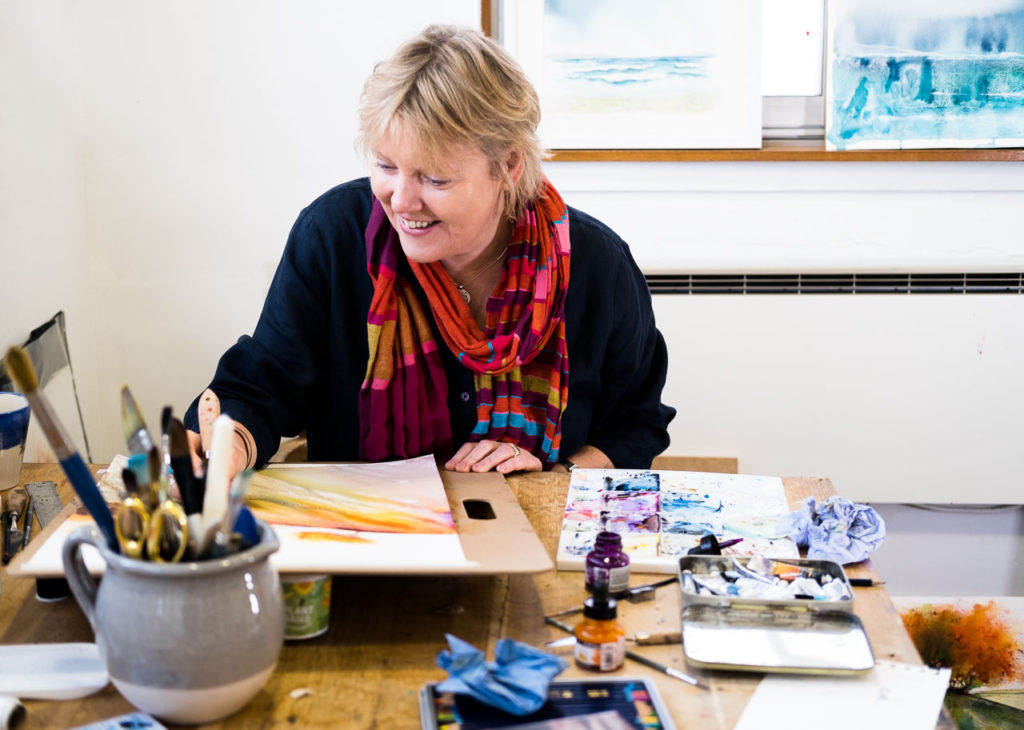 Artist Ione Harrison painting at her desk