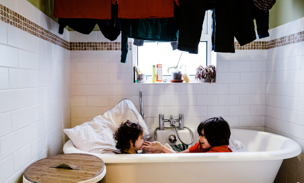 two children playing together in a bath fully clothed with laundry hanging above them North Yorkshire family photographer