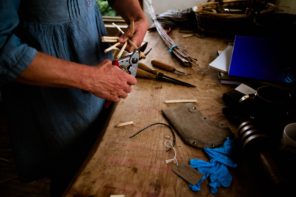 The hands of a woman in a blue dress using tools to cut willow for basket making