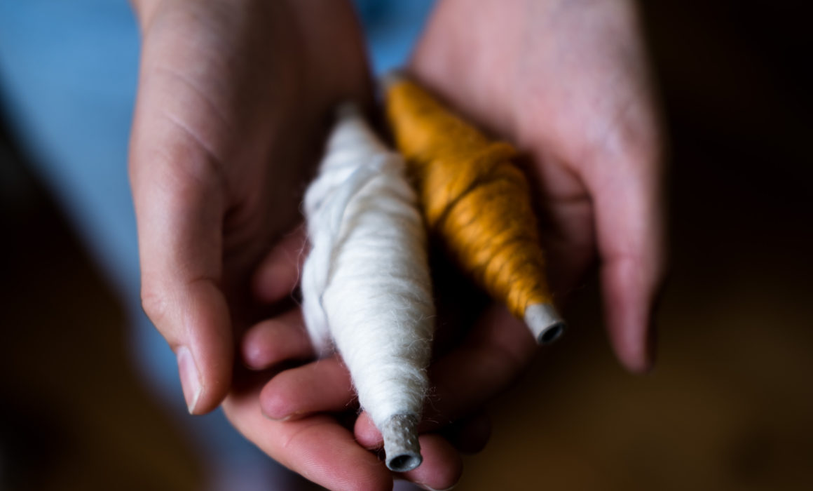 white hands holding two boobins of wool, one orange and one cream