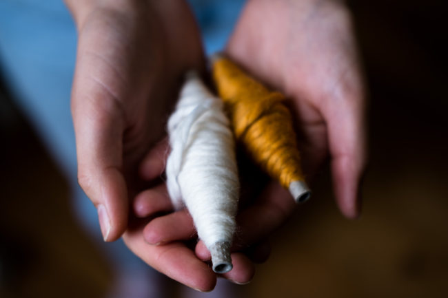 white hands holding two boobins of wool, one orange and one cream