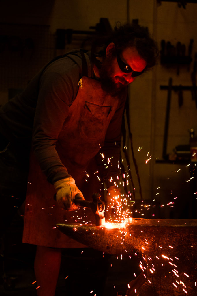 Blacksmith working at an anvil with glowing red sparks flying off