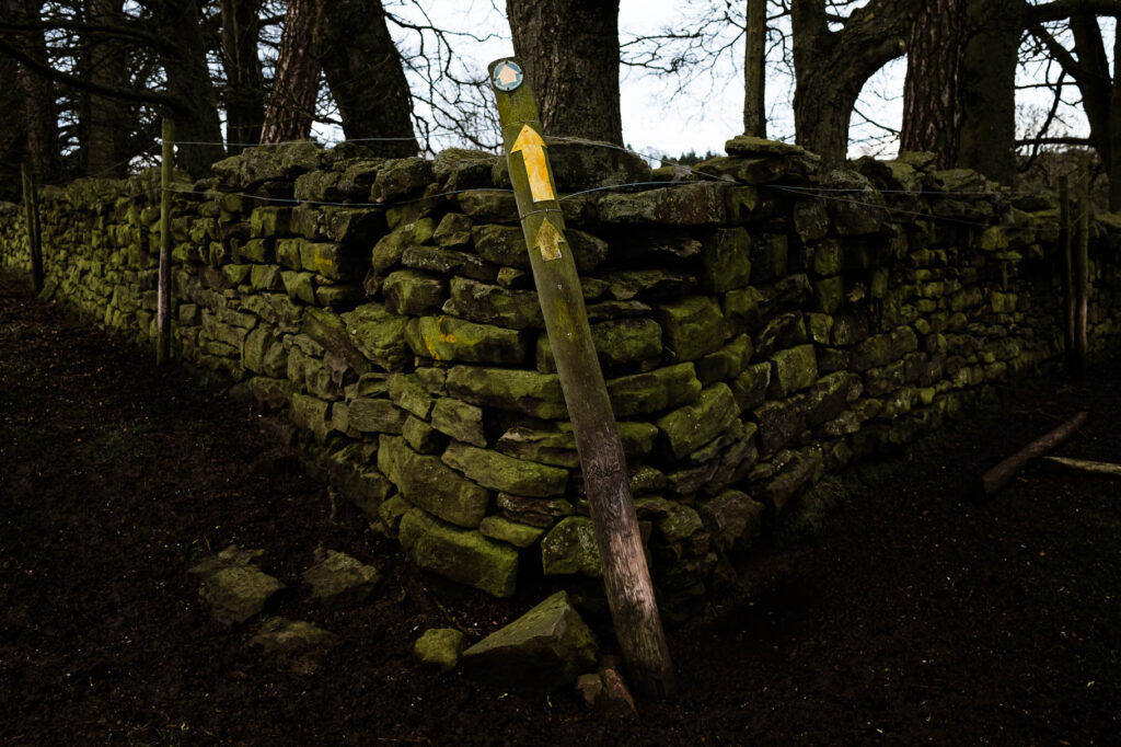 Photographic work exploring trespass and right to roam North Yorkshire. Image of waymarker on North York Moors with yellow arrow against a dry stone wall