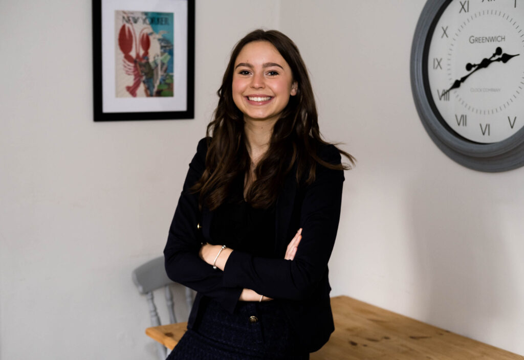 young wite woman with long dark hair in black blazer with painting behind professional headshot