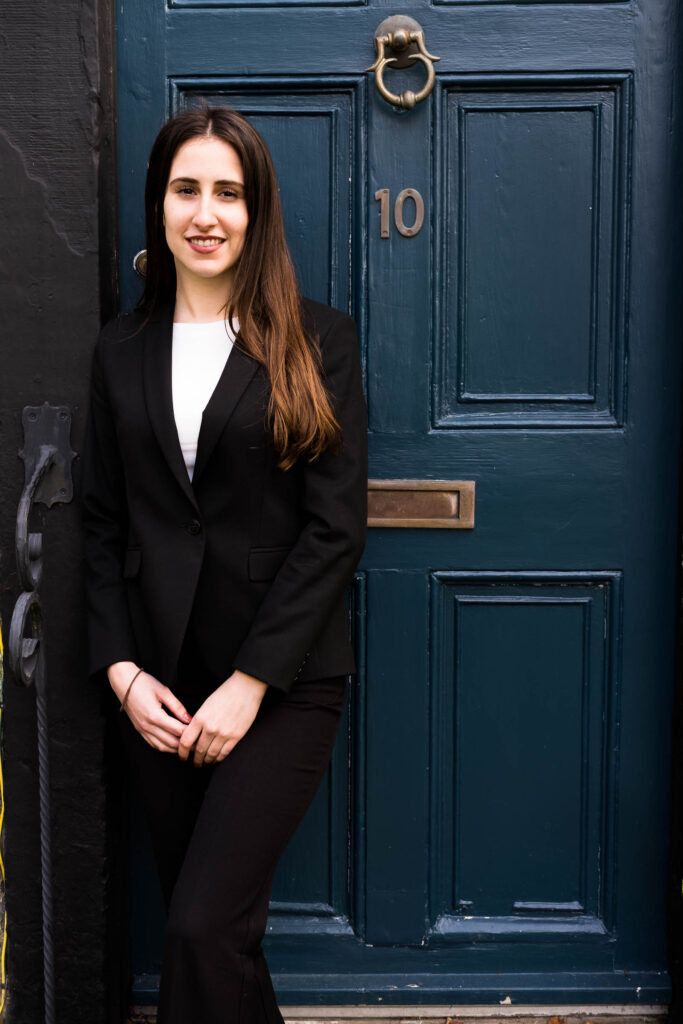 white woman with long dark hair in business suit against a blue door professional headshot