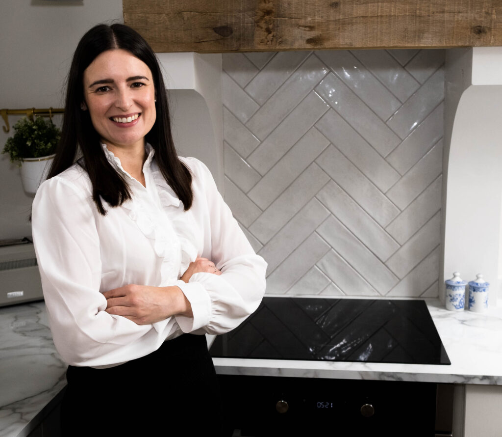 white woman with black hair and white blouse leaning against a kitchen counter professional headshot